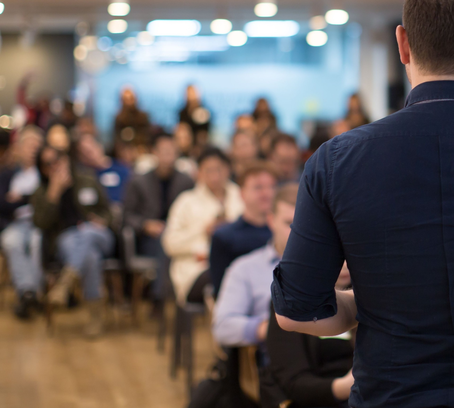 Conference photo audience and speaker giving speech. Seminar presenter on a panel during forum. Corporate manager in sales executive training discussion on stage. Investor pitch presentation.